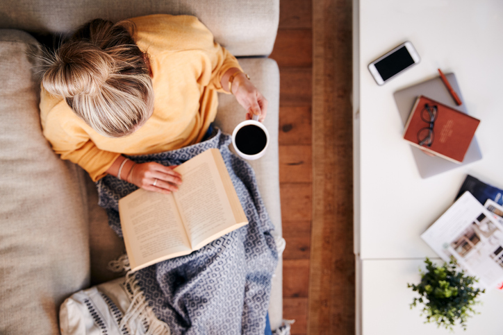 Young woman reasding a novel with a cup of coffee in hand - bird's eye view