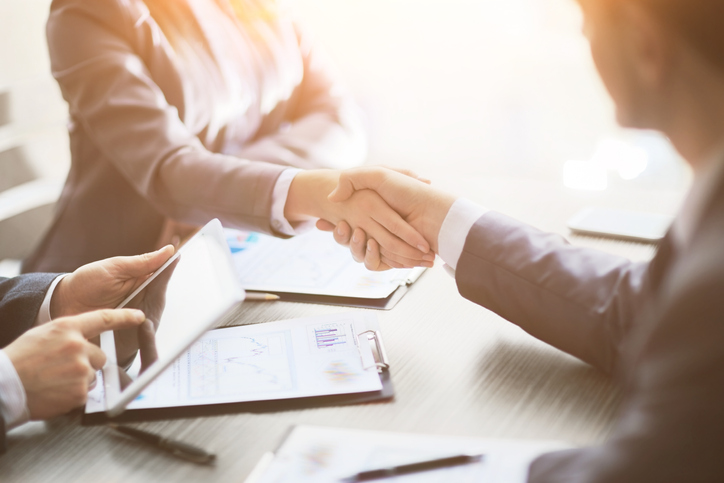 A man and women shake hands across a table at a business meeting