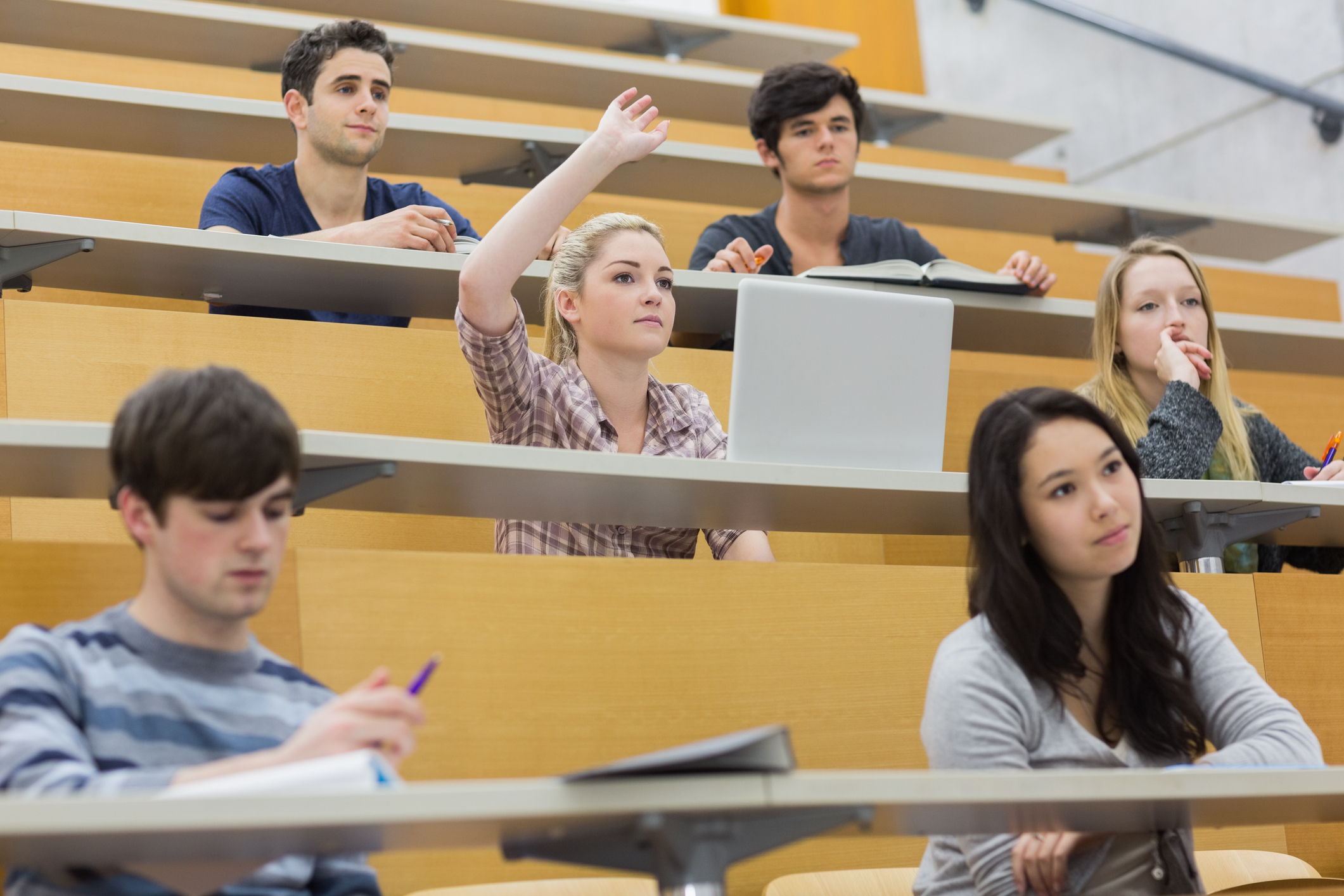 A group of students sit in a lecture theatre with a girl raising her hand to ask a question